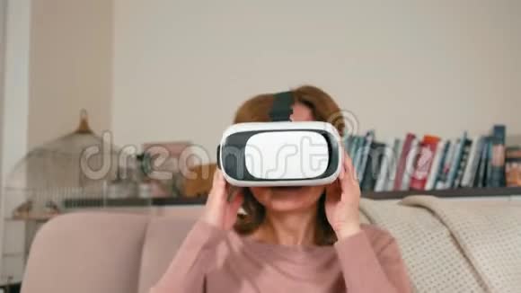 成年女士使用VR眼镜坐在沙发上在家玩电子游戏视频的预览图