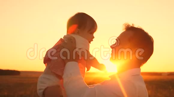 爸爸手中的漂亮女儿在灿烂的夕阳下微笑快乐爸爸在一个夏天的晚上在公园里和宝宝玩视频的预览图