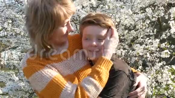 一位中年成年母亲在一个美丽繁茂背景下温柔地拥抱和亲吻她的少年儿子视频的预览图