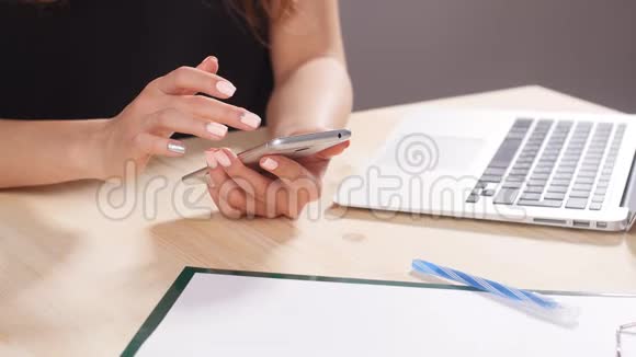 一个女孩正在办公室里用智能手机在电脑后面工作视频的预览图