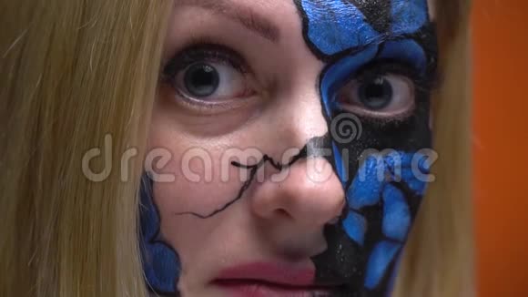 一个脸上画着蝴蝶形状的体画的女孩在镜头里显得很尴尬动作很慢视频的预览图