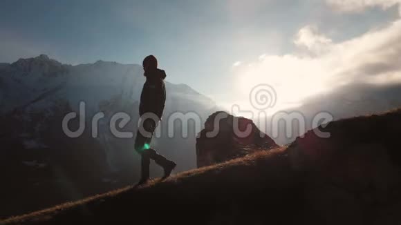 在美丽的日落中一个人在山的边缘行走的史诗般的照片的鸟瞰剪影视频的预览图