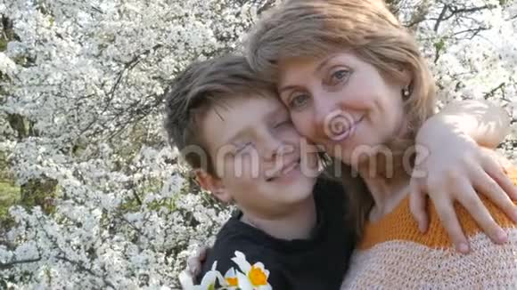 一位中年成年母亲在一个美丽繁茂背景下温柔地拥抱和亲吻她的少年儿子视频的预览图