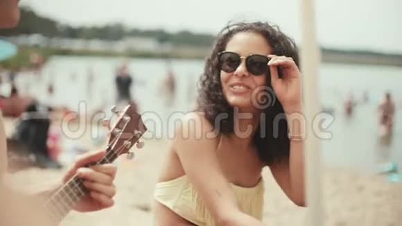 穿比基尼的年轻女人和朋友坐在海滩上微笑的肖像视频的预览图