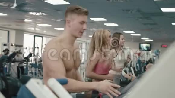 三位运动型的女性和男性正在现代健身房的跑步机上热身4K录像视频的预览图