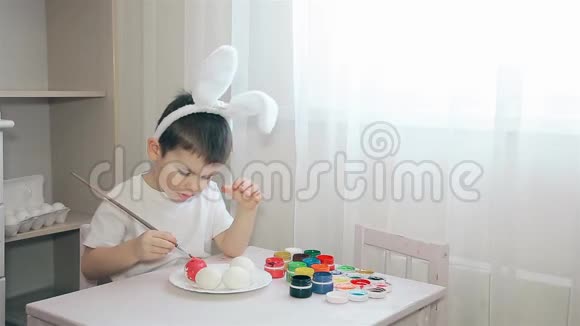 一个头上戴着兔子耳朵的孩子在画一个粉红色的复活节彩蛋视频的预览图