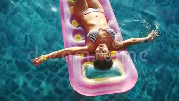 年轻迷人的微笑女人在游泳时在晶莹剔透的水中的充气床垫上享受夏天视频的预览图