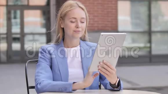 年轻女商人坐在户外用平板电脑视频的预览图