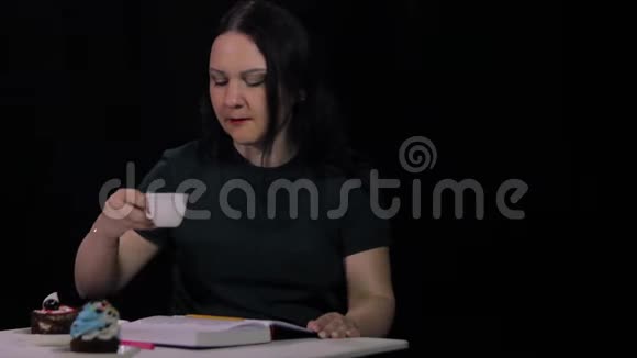 咖啡屋里的一个女人在黑色背景下喝着白色杯子里的咖啡写日记视频的预览图