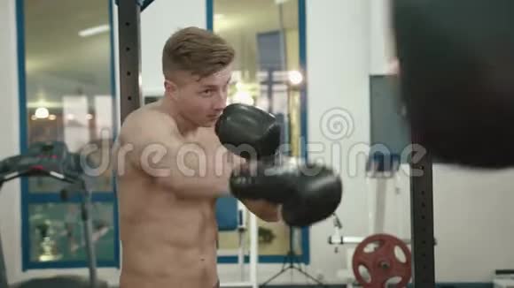 英俊的肌肉健美运动员的肖像赤裸的躯干拳击在现代健身房的一个拳击袋4k视频的预览图