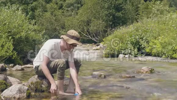 夏天爬山时旅行的人从山上的河里拿一瓶水视频的预览图