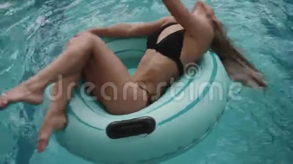 在豪华酒店的游泳池里一位穿着黑色比基尼的金发美女正在充气橡皮圈上旋转4公里视频的预览图