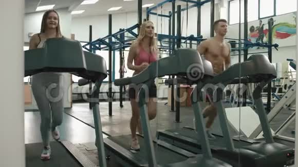 一名肌肉发达的男子和两名运动妇女正在现代健身房的跑步机上训练4K录像视频的预览图