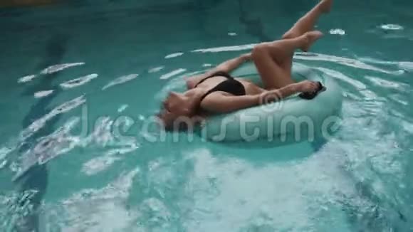 美丽的金发女人穿着黑色泳衣的完美身材正在游泳池里的充气橡胶圈上游泳4k视频的预览图