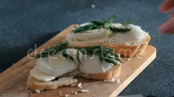 特写女人她的手拿着一个三明治上面有面包黄油鸡蛋和木板上的泔水然后咬它视频的预览图
