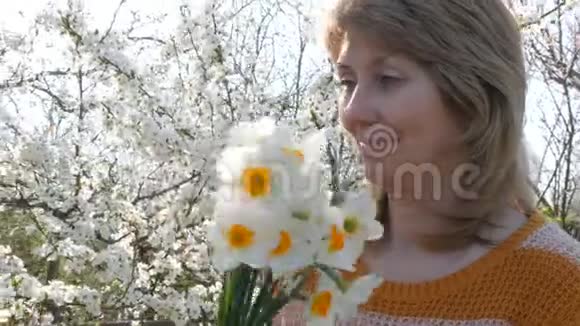 一个少年儿子在一棵盛开的树的背景上送给一个成年中年母亲一束白色水仙花视频的预览图