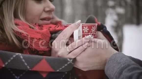 可爱的夫妻在冬天的森林里喝红杯子里的茶冬天两个情人在森林里散步视频的预览图