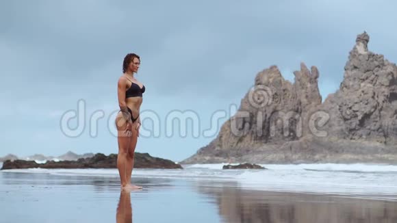 一个穿着泳衣的年轻苗条金发女孩戴着黑色大耳机听音乐在热带海滩上跳舞视频的预览图