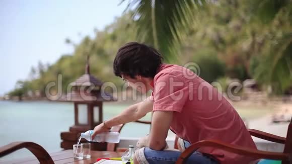 帅哥在海滩上的咖啡馆里倒水喝水1920x1080视频的预览图