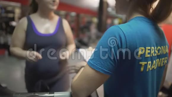 胖女人在健身房和私人教练一起锻炼在跑步机上锻炼视频的预览图