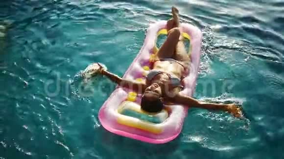 日落时分年轻漂亮的女人在游泳池里用透明的水晶水在充气床垫上享受夏天视频的预览图