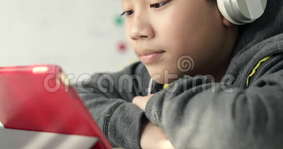 年轻的亚洲男孩在家玩带耳机的平板电脑多莉出去了视频的预览图