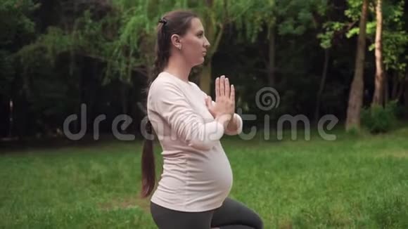 孕妇在公园里做瑜伽的地毯上站在一条腿上的姿势体式树式视频的预览图
