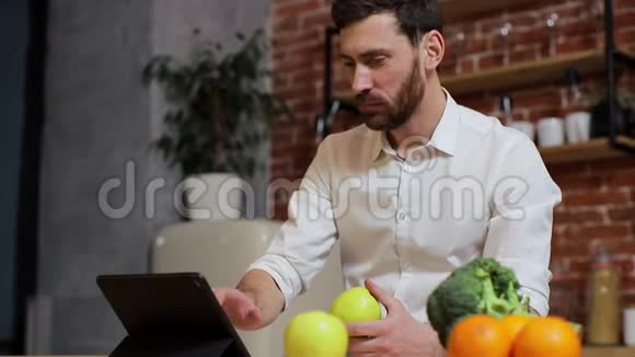 男人在家庭厨房的平板电脑上浏览英俊的年轻人在平板电脑上浏览微笑着快乐一个男人吃视频的预览图