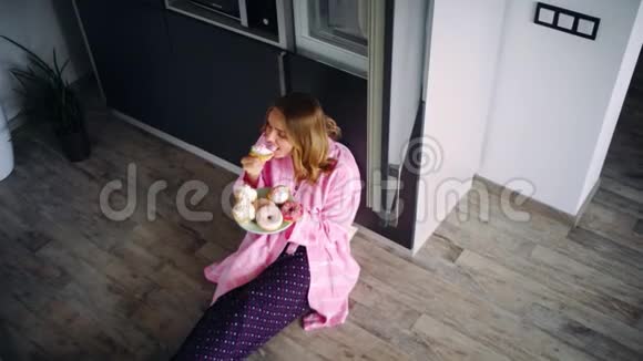 漂亮的女人坐在厨房的地板上吃糖果满意的女孩视频的预览图