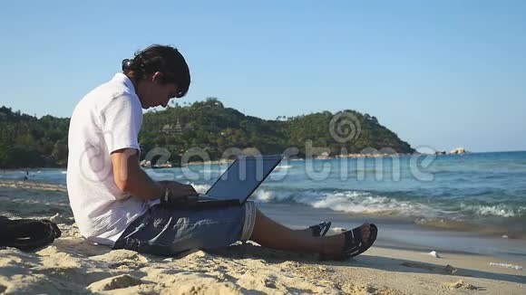 商人自由职业者坐在沙滩上用笔记本电脑工作慢动作1920x1080视频的预览图