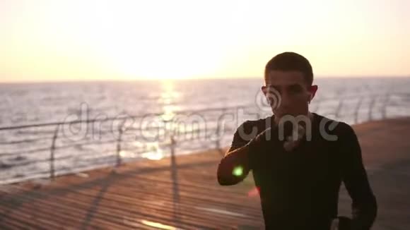 清晨一位身穿黑色衬衫的男拳击手在海前长廊上训练时的正面景色视频的预览图