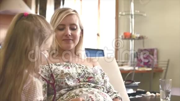 怀孕的母亲和女儿正坐在家里的沙发上一个小女儿听着孩子从母亲在视频的预览图