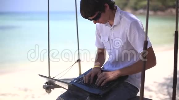 一个人坐在秋千上在笔记本电脑上工作在异国情调的海滩上1920x1080视频的预览图