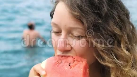 一个美丽的卷发女人在海上咬掉一片西瓜的肖像视频的预览图
