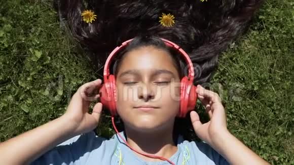 有魅力的女孩留着长长的黑发躺在公园的草地上听着耳机里的音乐心情很好视频的预览图