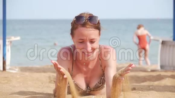 美丽的女人躺在海滩上从她的手里倒沙子沙滩快乐的女人躺在沙滩上日光浴视频的预览图