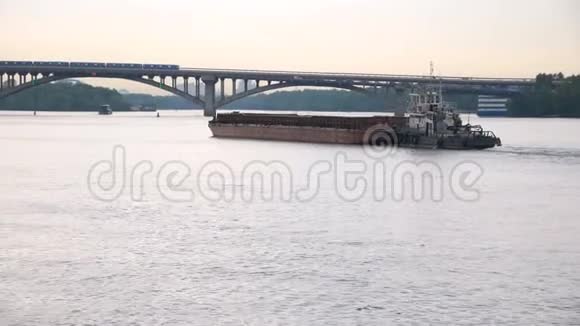 一艘小船拖着一艘驳船船上的货物朝桥的方向行驶视频的预览图