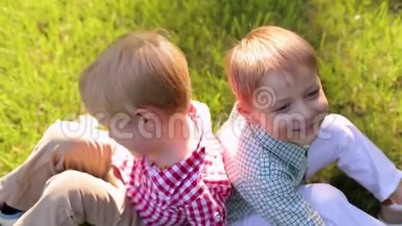 两个有趣的小男孩在公园的草地上玩耍他们坐在草地上视频的预览图