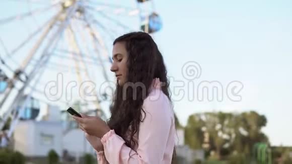 女孩走在摩天轮旁使用智能手机4K视频的预览图