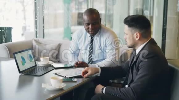 两个有信心的商人看着笔记本电脑上的图表讨论财务报告和视频的预览图