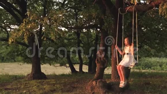 小女孩在阳光下的树下荡秋千和孩子们一起玩特写镜头家庭乐趣在大自然中儿童游乐设施视频的预览图