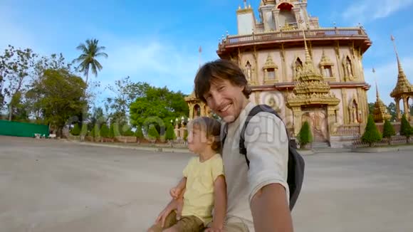 一名年轻人和他的儿子在普吉岛的一座瓦查龙佛教寺庙前自拍的慢镜头视频的预览图