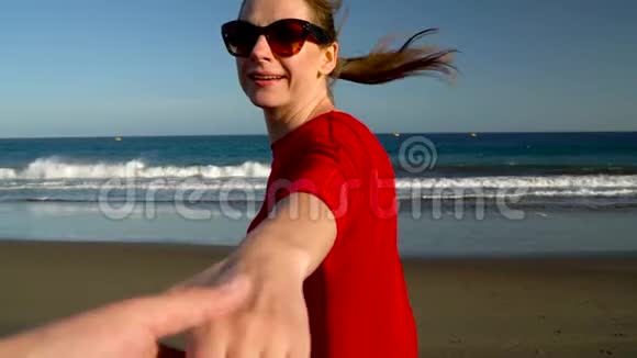 跟着我快乐的年轻女人穿着红色的衣服拉着男人手手牵手走到海边的海边视频的预览图