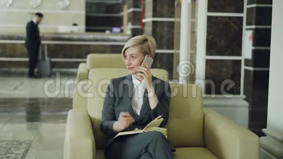 有魅力的女商人坐在扶手椅上拿着记事本说话商人拿着行李走路视频的预览图
