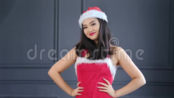 戴着圣诞老人帽子和西装微笑着在演播室摆姿势的亚洲美女画像视频的预览图
