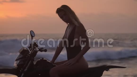 身着黑色比基尼的美女摆姿骑着汽车摩托车傍晚的阳光染红了天空视频的预览图