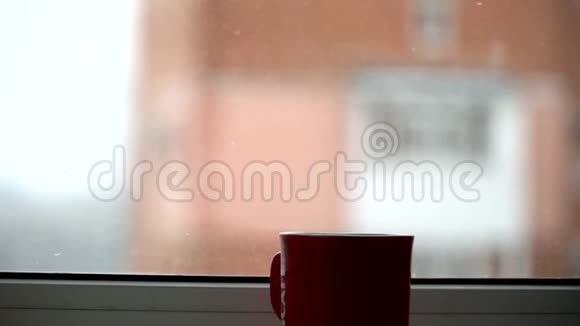 在白雪皑皑的冬天早晨的圣诞节背景下热气腾腾的茶杯站在窗户上视频的预览图
