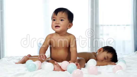 两个婴儿在床上一个在玩彩球一个在睡觉视频的预览图