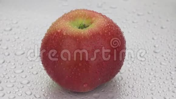 一整个成熟的苹果在一滴露水中旋转躺在白色的潮湿背景上视频的预览图