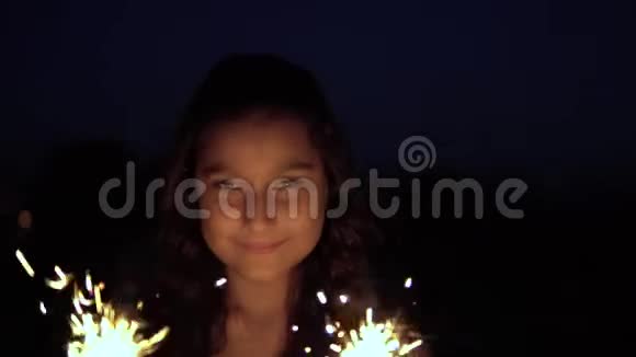 一位留着深色长发的年轻女子在城市的背景下晚上放烟火很高兴有一个好的视频的预览图